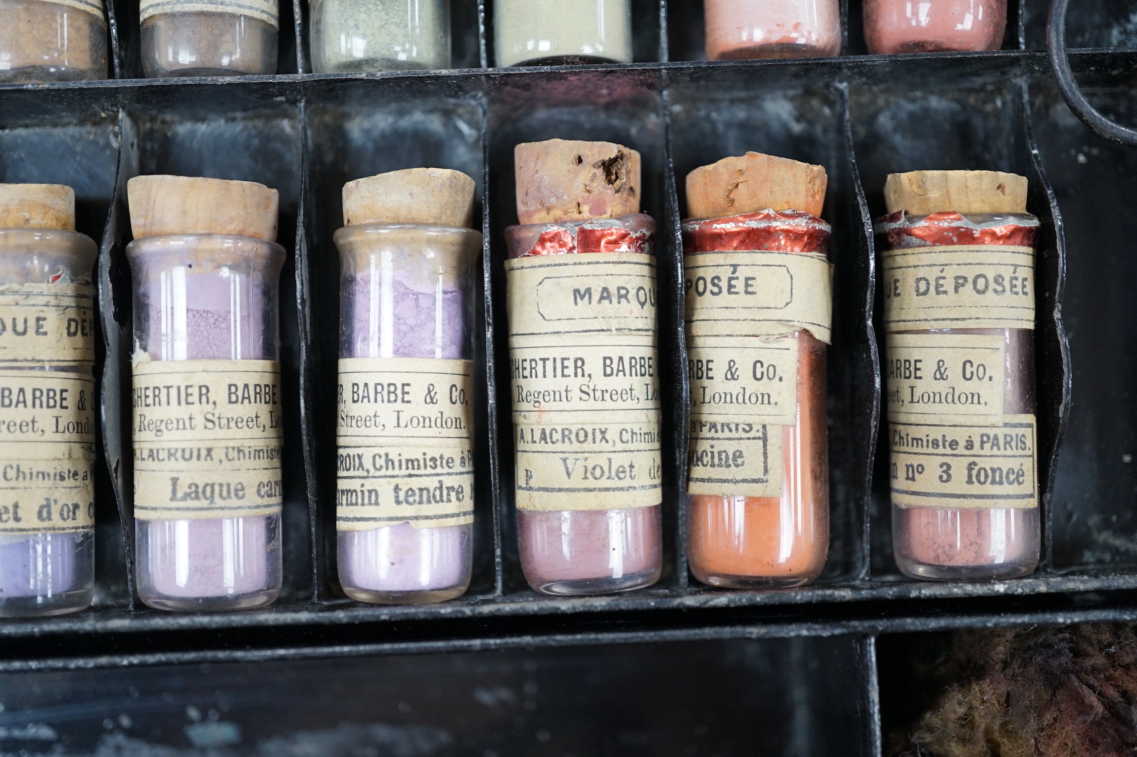 A black artist's tin box, with fitted interior, containing glass phialls of coloured shades of powdered paint and a white glass samples panel etc, box 37.5cm wide, 27cm deep